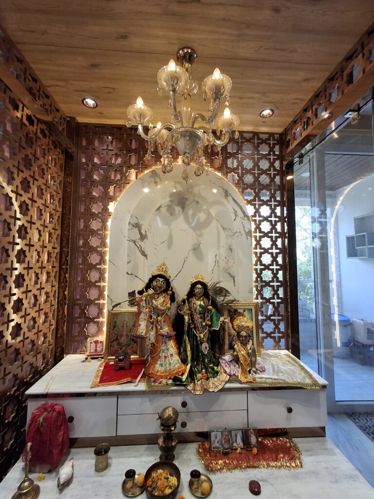 luxury pooja room mandir design Kolkata marble backdrop jaali partition Radha Krishna temple storage unit chandelier lighting