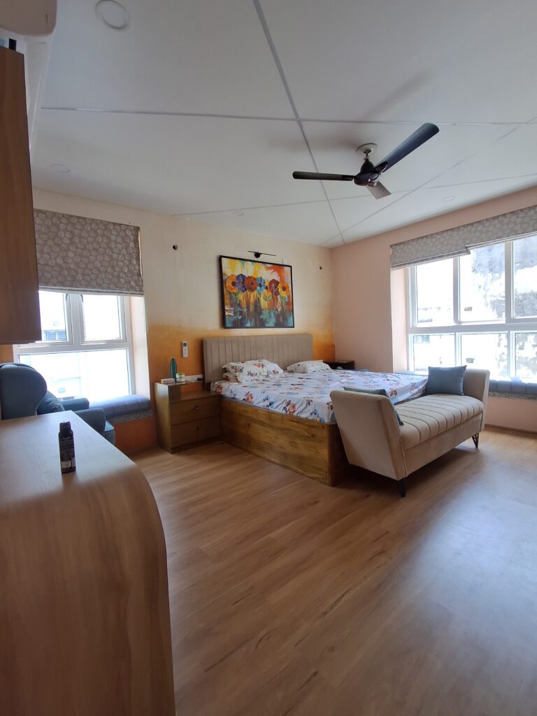 luxury master bedroom interior design Kolkata ombre peach wall wooden flooring bay window seating upholstered headboard settee natural light